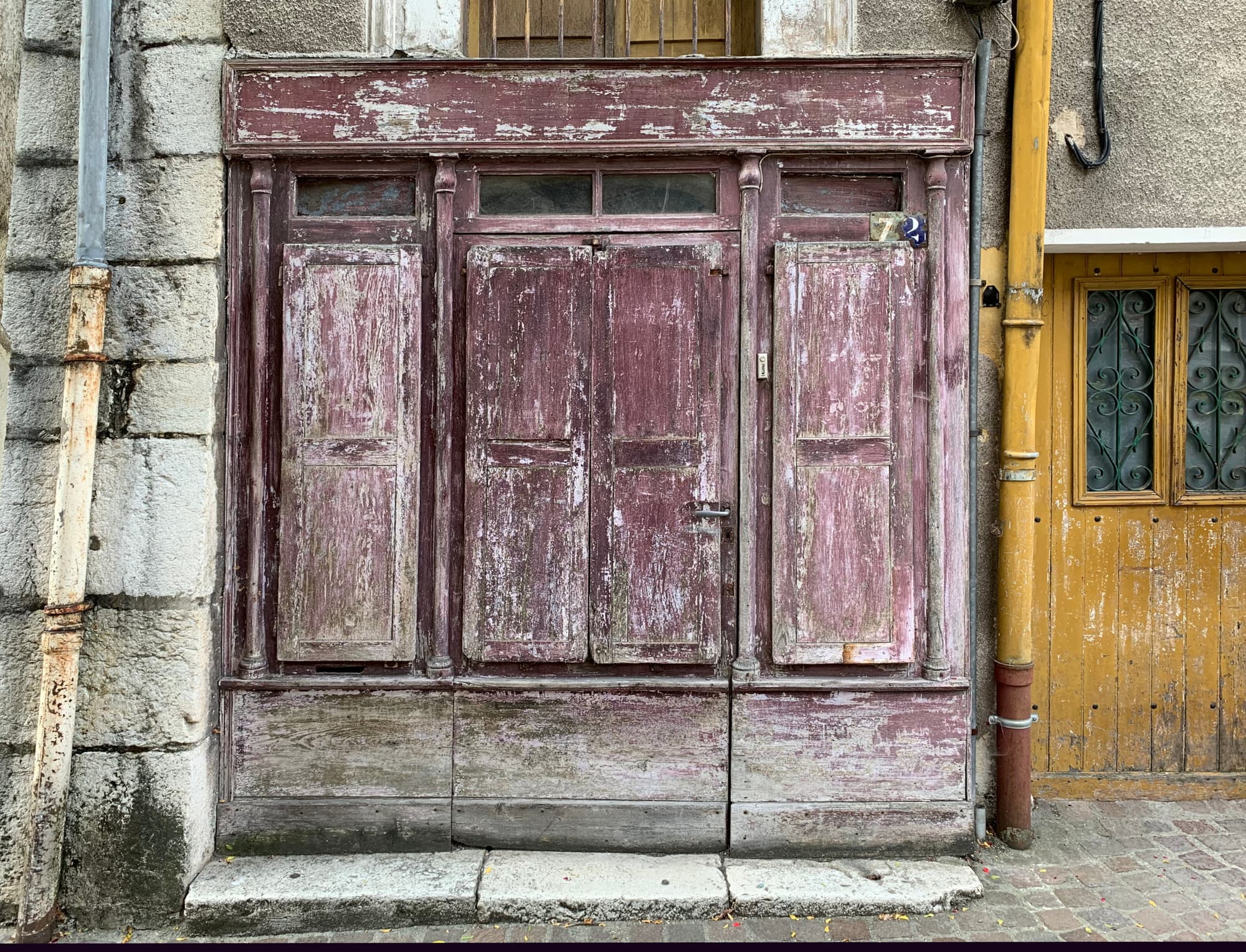 Devanture ancienne fermée par des volets pleins en bois à côté d'une porte d'entrée