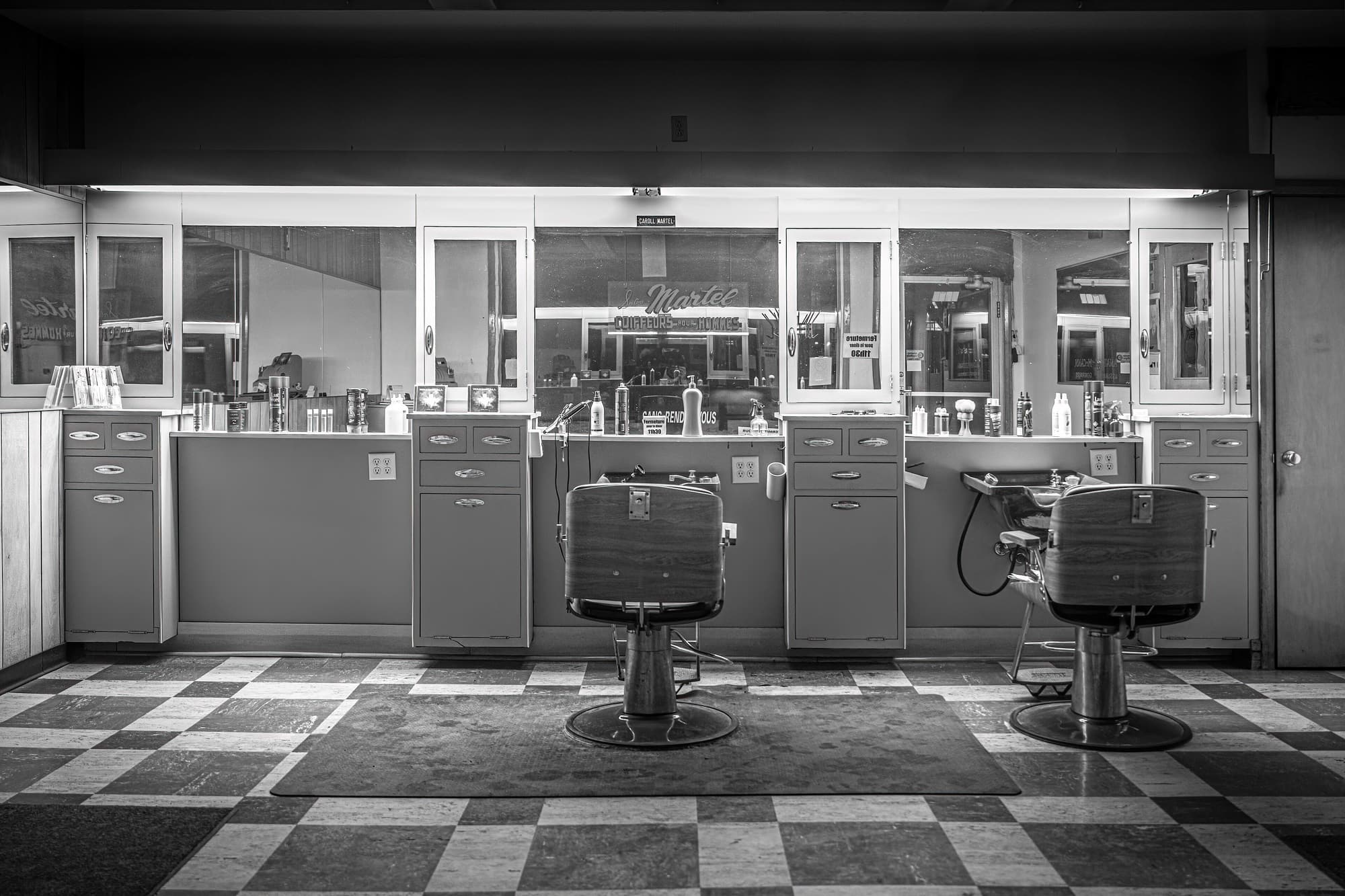 Salon de barbier équipé de fauteuils, de miroirs et de meubles de rangement, en noir et blanc